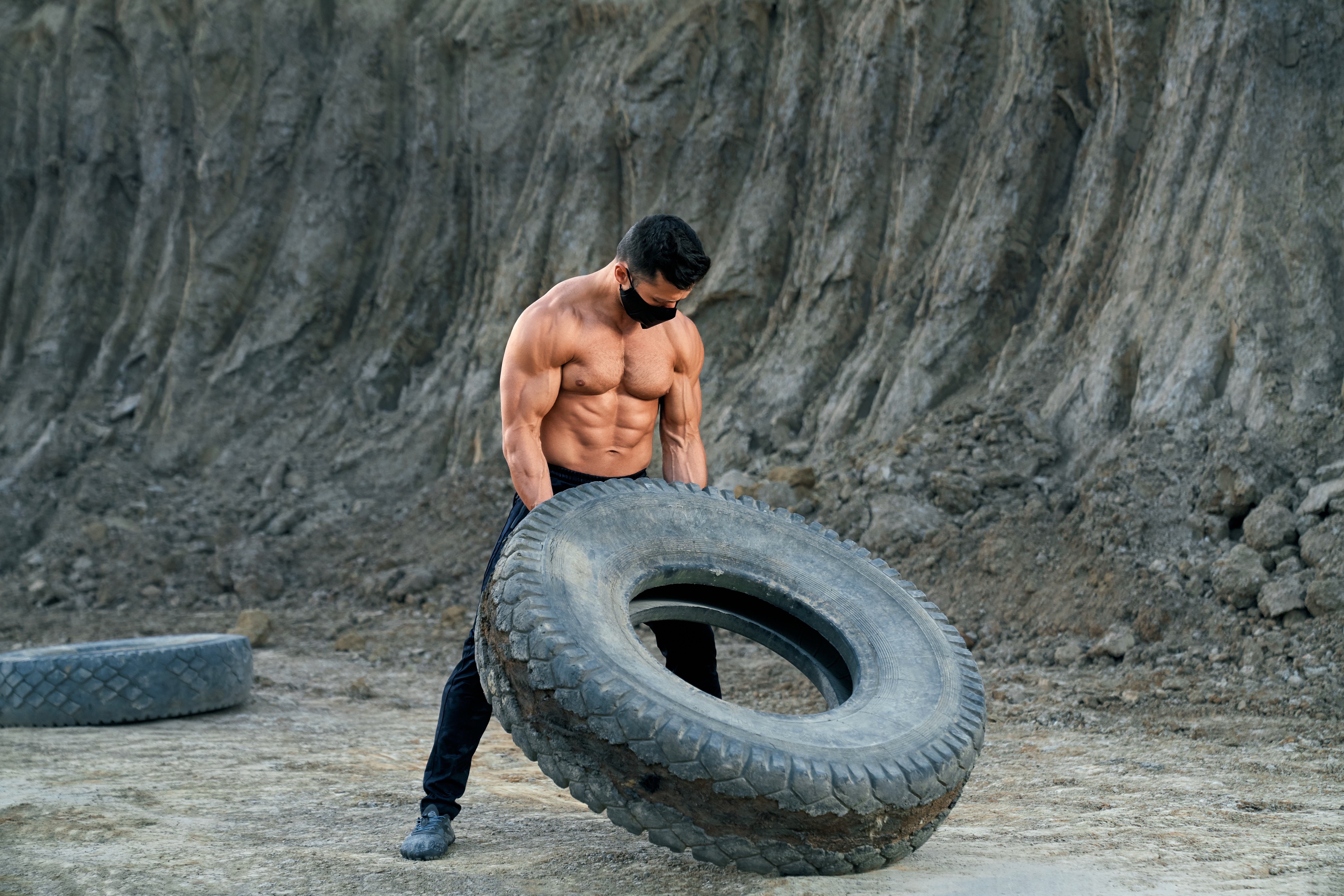 Bodybuilder in black mask doing exercises with large wheel
